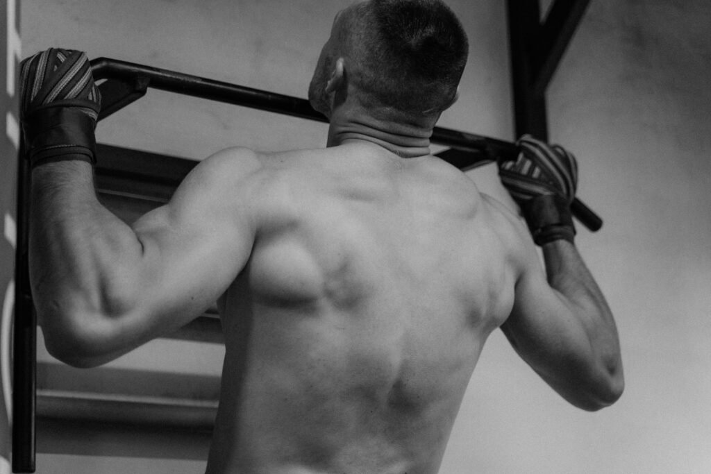 This image depicts a man maximizing his back gains by doing pull ups.